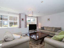 A living room with two beige sofas a dark wooden coffee table a television on a stand and windows with patterned curtains at The Coach House in Castle Cary