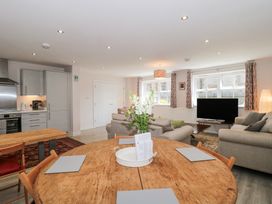 An open-plan living room and kitchen with a round wooden dining table and chairs a sofa set a television and windows with curtains at The Coach House in Castle Cary