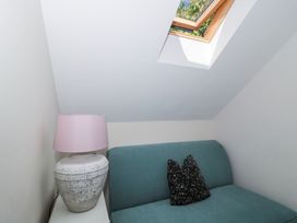 A teal sofa with a black pillow next to a white side table with a lamp under a skylight window at The Coach House in Castle Cary