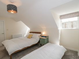 A bedroom with two single beds a green nightstand with a lamp and a window with blinds at The Coach House in Castle Cary