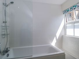 A bathroom with a bathtub shower and a window with a patterned blind at The Coach House in Castle Cary