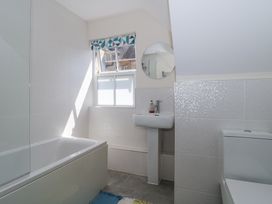 A bathroom with a bathtub a sink a round mirror a toilet and a window with a patterned blind at The Coach House in Castle Cary