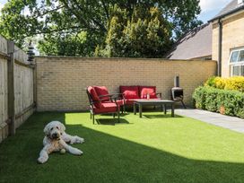 A backyard with artificial grass a sitting area with red cushions a table a small fireplace and a dog laying on the grass at The Coach House in Castle Cary