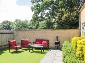 An outdoor patio area with red cushioned chairs and a sofa around a black table with a bottle and glasses a chiminea a brick wall and green plants at The Coach House in Castle Cary