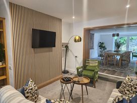 A living room with a wall mounted tv a green armchair two round wooden tables and a view into a dining room at Moss Crag in Glenridding