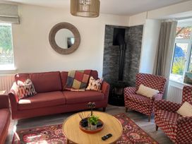 A living room with red sofas armchairs round wooden coffee table and a stove at Moss Crag in Glenridding