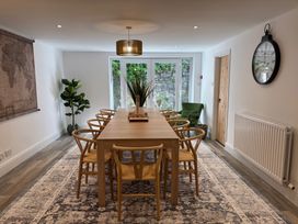 A dining room with a wooden table and eight chairs a large wall clock and a plant at Moss Crag in Glenridding