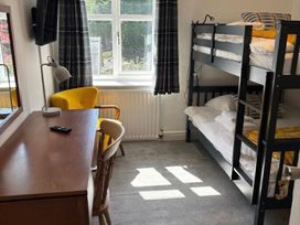 A bedroom with a bunk bed, a wooden desk with a lamp, a yellow armchair, and a window with curtains at Moss Crag in Glenridding