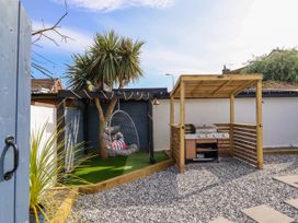 A garden with a hanging chair under a pergola and a barbecue grill under a wooden shelter at Fishermans Cottage in Prestatyn