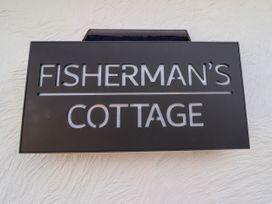 A black sign with cut-out letters spelling Fisherman's Cottage mounted on a textured white wall at Fishermans Cottage in Prestatyn