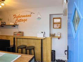A small kitchen area with wooden counter stools a blue door and a wall sign reading Fishermans Cottage at Fishermans Cottage in Prestatyn
