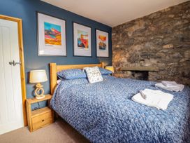 A bedroom with a blue bedspread a wooden headboard stone wall and framed pictures at Fishermans Cottage in Prestatyn