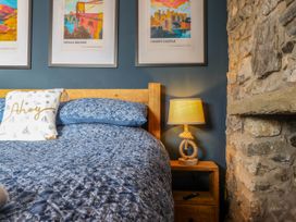 A bedroom with a wooden bed frame a blue quilt and pillows a wooden nightstand with a lamp and a stone wall at Fishermans Cottage in Prestatyn