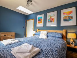 A bedroom with a blue quilted bedspread white towels a wooden dresser framed artwork and two lamps at Fishermans Cottage in Prestatyn