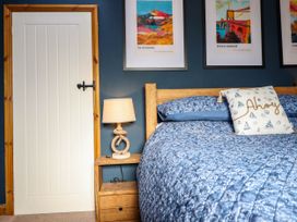 A bedroom with a wooden bed and blue bedding a wooden nightstand with a rope lamp and framed artwork on a blue wall at Fishermans Cottage in Prestatyn