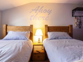 A bedroom with two wooden twin beds a wooden nightstand with a lamp and a remote control between them and wall decor with the words Ahoy there at Fishermans Cottage in Prestatyn