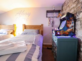A bedroom with two single beds a lamp a small arcade game machine on a chest of drawers and a stone wall at Fishermans Cottage in Prestatyn