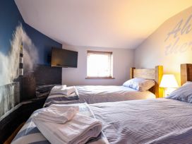 A bedroom with two single beds with striped bedding a wall-mounted television and a window at Fishermans Cottage in Prestatyn