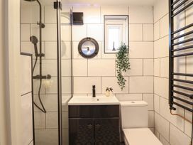 A bathroom with a shower area glass door sink cabinet toilet small window and black towel radiator at Fishermans Cottage in Prestatyn