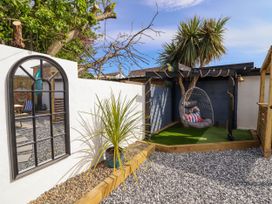 A garden area with a hanging chair under a pergola and a large mirror on a white wall at Fishermans Cottage in Prestatyn