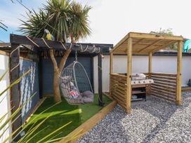 An outdoor area with a hanging chair on artificial grass and a covered barbecue on gravel at Fishermans Cottage in Prestatyn