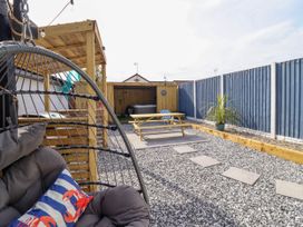 A backyard with a hanging egg chair a wooden pergola a picnic table a decking area and a blue fence at Fishermans Cottage in Prestatyn