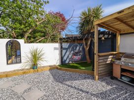 An outdoor garden area with a hanging chair, barbecue grill, stepping stones, and a white wall with a mirror at Fishermans Cottage in Prestatyn