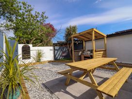 An outdoor space with a wooden picnic table a covered barbecue grill swing chair and plants at Fishermans Cottage in Prestatyn
