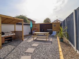 An outdoor patio area with a wooden picnic table, barbecue grill under a wooden canopy, and a seating area with a hot tub at Fishermans Cottage in Prestatyn