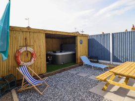 A backyard with a wooden shelter containing a hot tub two striped deck chairs a picnic table and a red and white life ring at Fishermans Cottage in Prestatyn