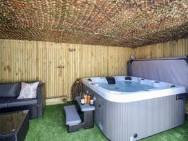 A covered outdoor area with a hot tub and rattan sofa on artificial grass at Fishermans Cottage in Prestatyn