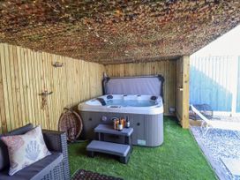 An outdoor covered area with a hot tub a wicker chair a small sofa with a pillow artificial grass and wooden panel walls at Fishermans Cottage in Prestatyn