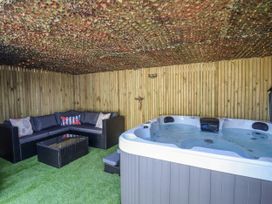An outdoor seating area with a sectional sofa and hot tub under a camouflage net at Fishermans Cottage in Prestatyn