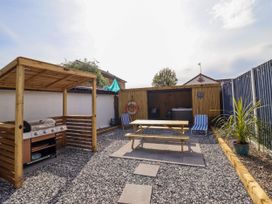 An outdoor area with a covered barbecue grill a picnic table two striped chairs and a hot tub under a wooden shelter at Fishermans Cottage in Prestatyn