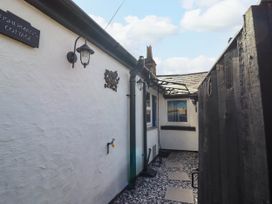A narrow outdoor pathway with white walls black rain gutters a black fence and stepping stones at Fishermans Cottage in Prestatyn