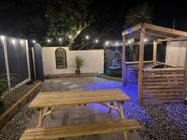 An outdoor patio area with a wooden picnic table a wooden pergola with a grill and a hanging chair surrounded by string lights at Fishermans Cottage in Prestatyn