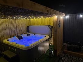 A hot tub with blue water and lighting under string lights in a wooden enclosure at Fishermans Cottage in Prestatyn