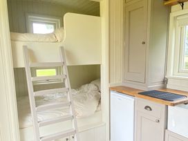A small bedroom with bunk beds and a ladder next to a compact kitchen area at Shepherds Hut 2 in Northchapel