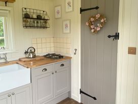 A kitchen corner with wooden countertop ceramic sink gas stove and grey cabinets with a door decorated with a floral wreath at Shepherds Hut 2 in Northchapel