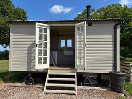 A small wooden shepherds hut with open double doors showing a kitchenette inside at Shepherds Hut 2 in Northchapel