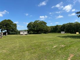 A grassy field with three small wooden huts and trees in the background at Shepherds Hut 2 in Northchapel
