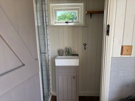 A small bathroom with a sink cabinet a mirror a window and a light switch at Shepherds Hut 2 in Northchapel