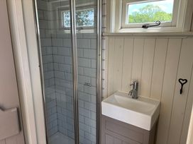 A bathroom with a tiled shower enclosure and a white sink under a window at Shepherds Hut 2 in Northchapel