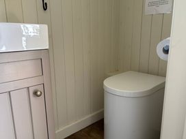 A small bathroom with a modern toilet and a sink cabinet with beige panelled walls at Shepherds Hut 2 in Northchapel