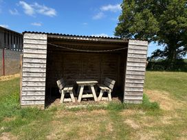 A wooden shelter with table and benches on grass near a tree at Shepherds Hut 2 in Northchapel