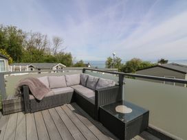 An outdoor balcony with a grey corner sofa and a glass topped table overlooking trees and buildings at Heulwen in New Quay