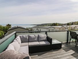 An outdoor deck with a sectional sofa and a side table overlooking caravans and a body of water at Heulwen in New Quay
