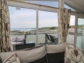 A seating area with a sofa and floral curtains facing a balcony with outdoor furniture and a view of mobile homes and hills at Heulwen in New Quay