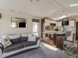 An open plan living room and kitchen with a sofa, mirror, countertop with stools, cabinets, and kitchen appliances at Heulwen in New Quay
