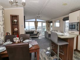 An open living space with a dining table set with plates and glasses a kitchen island with two bar stools a sofa and a glass door leading to a balcony with a view of the sea at Heulwen in New Quay
